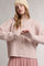 woman wearing a light pink oversized cardigan with buttons and a ribbed texture, styled with a pink polka dot skirt and a beige knit beanie