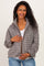 woman wearing a brown and white gingham patterned maternity jacket, gently holding her baby bump
