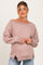 woman wearing a light pink oversized maternity sweater with boat neckline and ribbed texture, gently cradling her baby bump