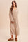 woman wearing a beige ribbed knit maxi sweater dress with long sleeves and a v-neckline, standing against a neutral background