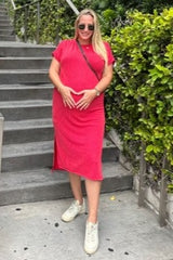 woman wearing a red maternity dress with ribbed texture and holding her baby bump while standing on stairs