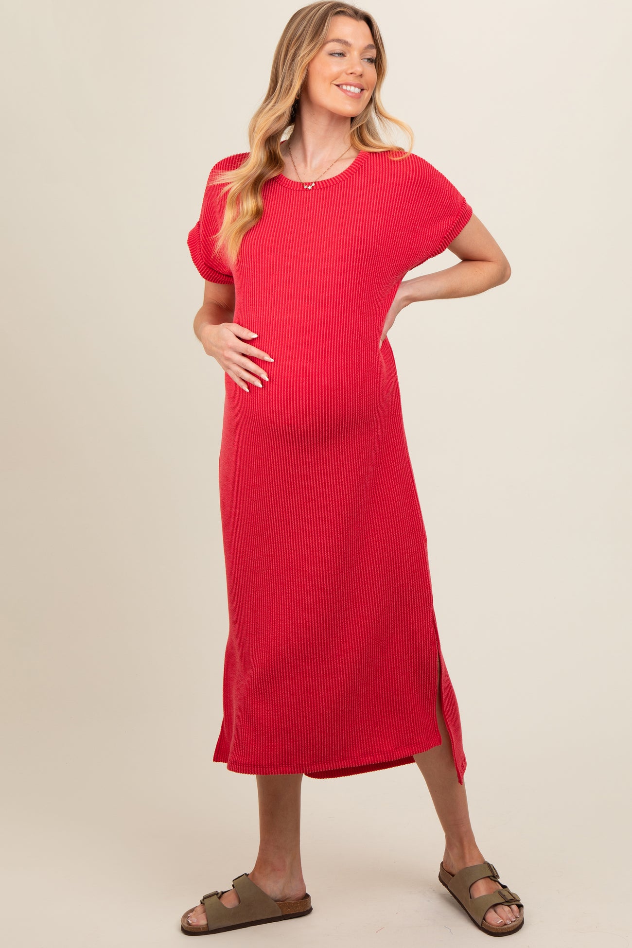 woman wearing a red ribbed maternity dress with short sleeves and side slits, holding her baby bump