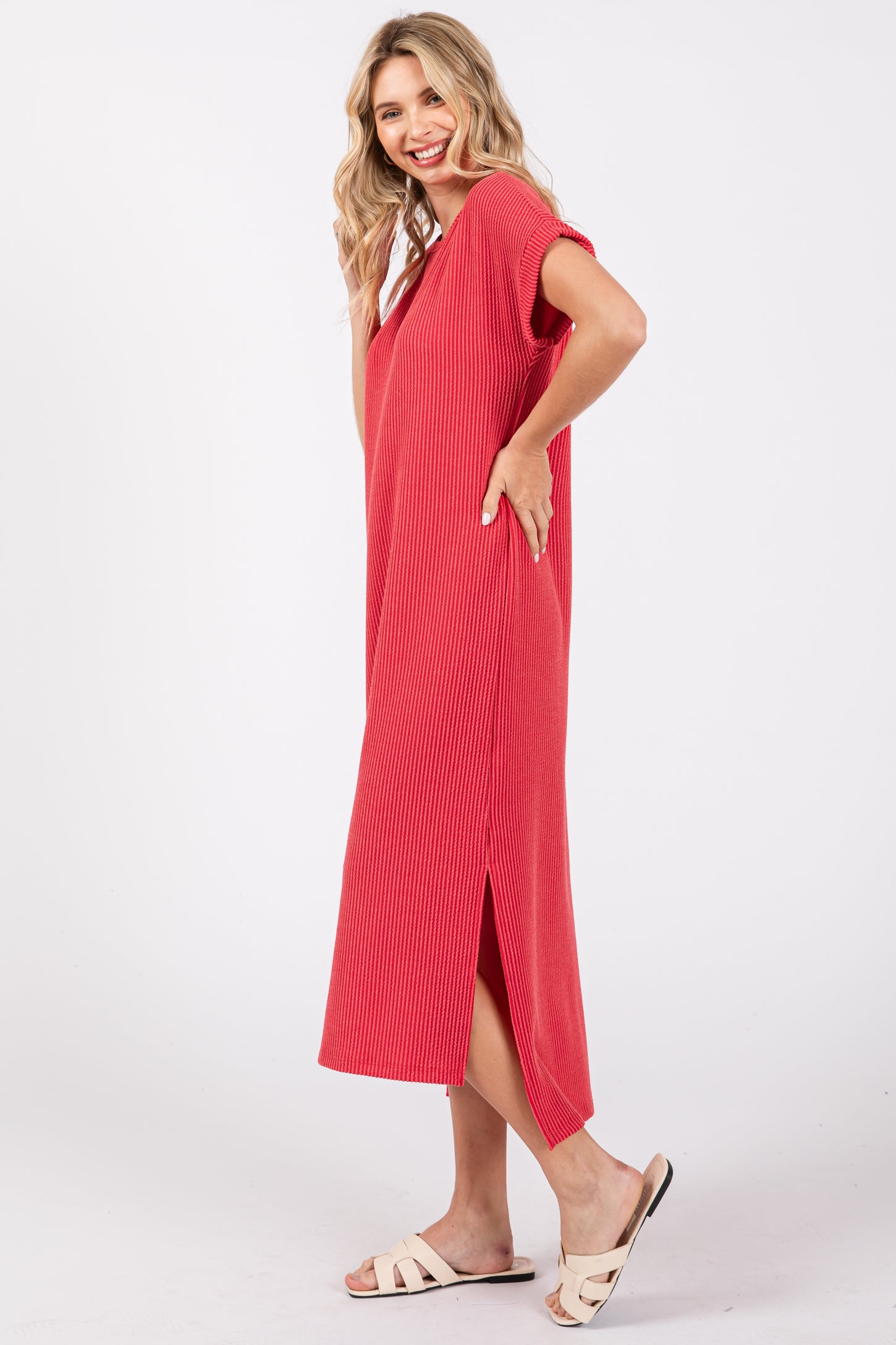woman wearing a red ribbed midi dress with short sleeves and side slits, smiling and posing with one hand on her hip