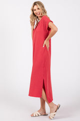 woman wearing a red ribbed midi dress with short sleeves and side slits, smiling and posing with one hand on her hip