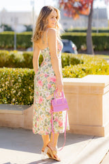 woman wearing a floral midi dress with spaghetti straps and holding a pink handbag