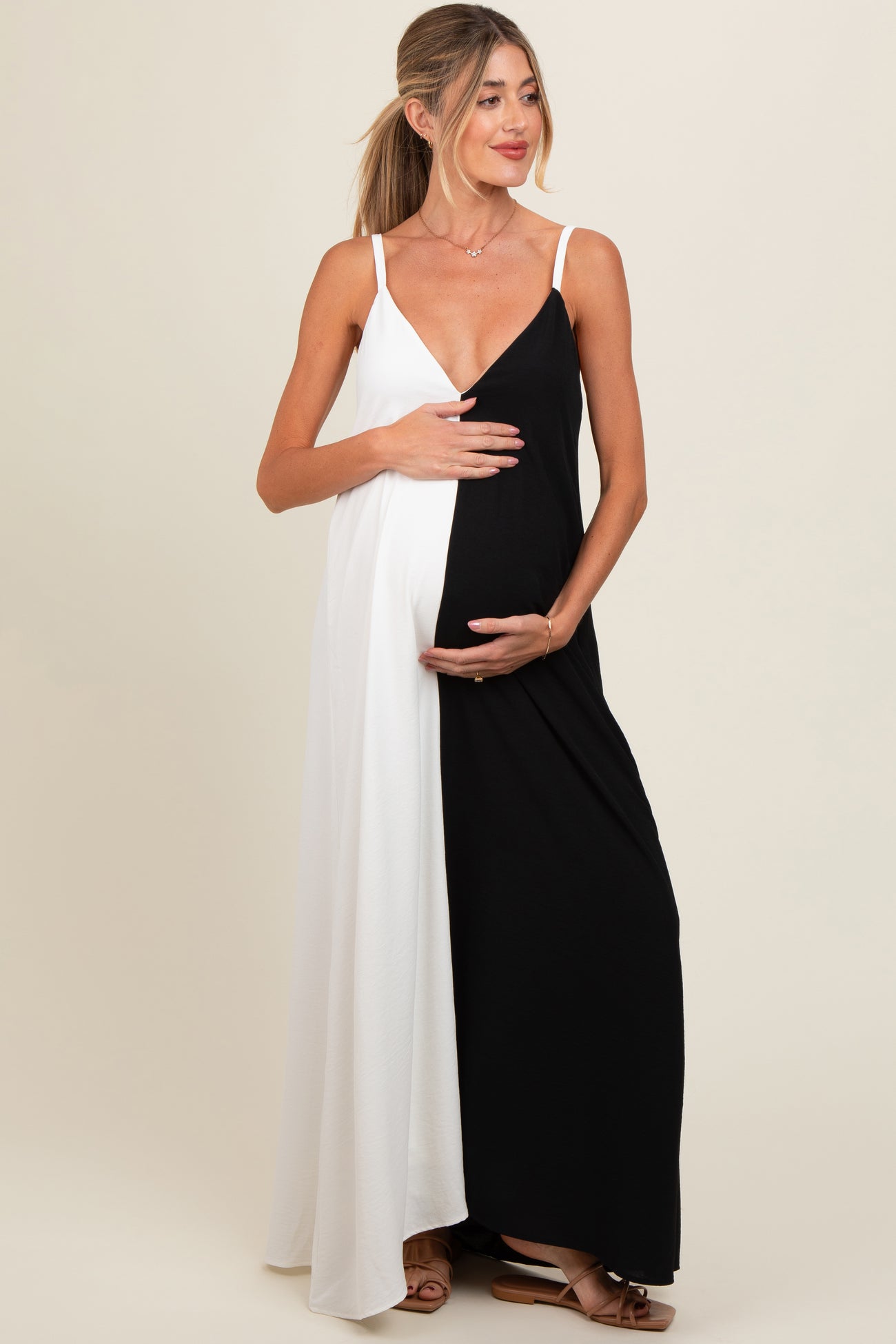 woman wearing a black and white maternity maxi dress, cradling her baby bump with one hand