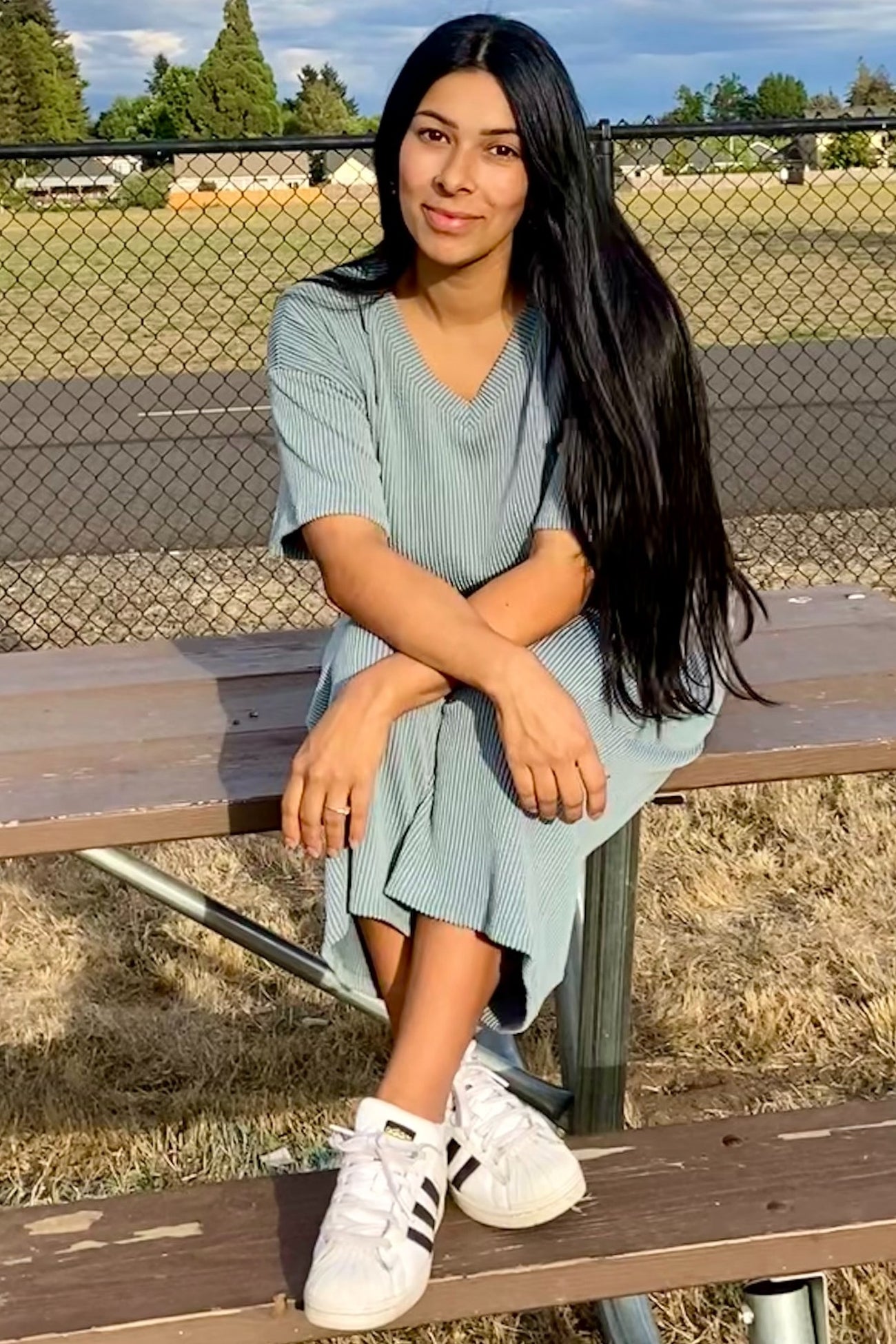 woman wearing a green and white striped midi dress and white sneakers, sitting on a bench outdoors