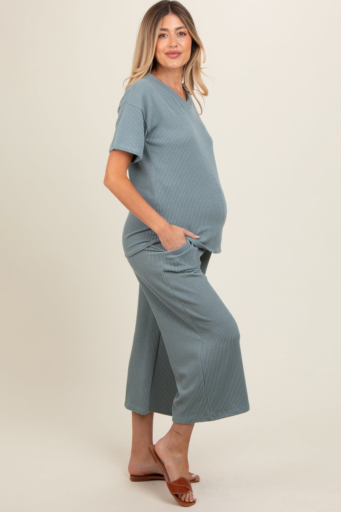 woman wearing a light blue maternity loungewear set with a short sleeve top and wide-leg pants, showing her baby bump