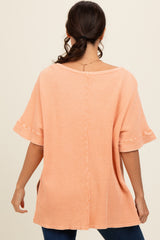 woman wearing a peach ribbed oversized top with short ruffled sleeves and a button detail running down the back
