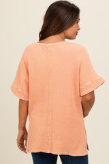 woman wearing a light orange short sleeve maternity top with a relaxed fit and side slits