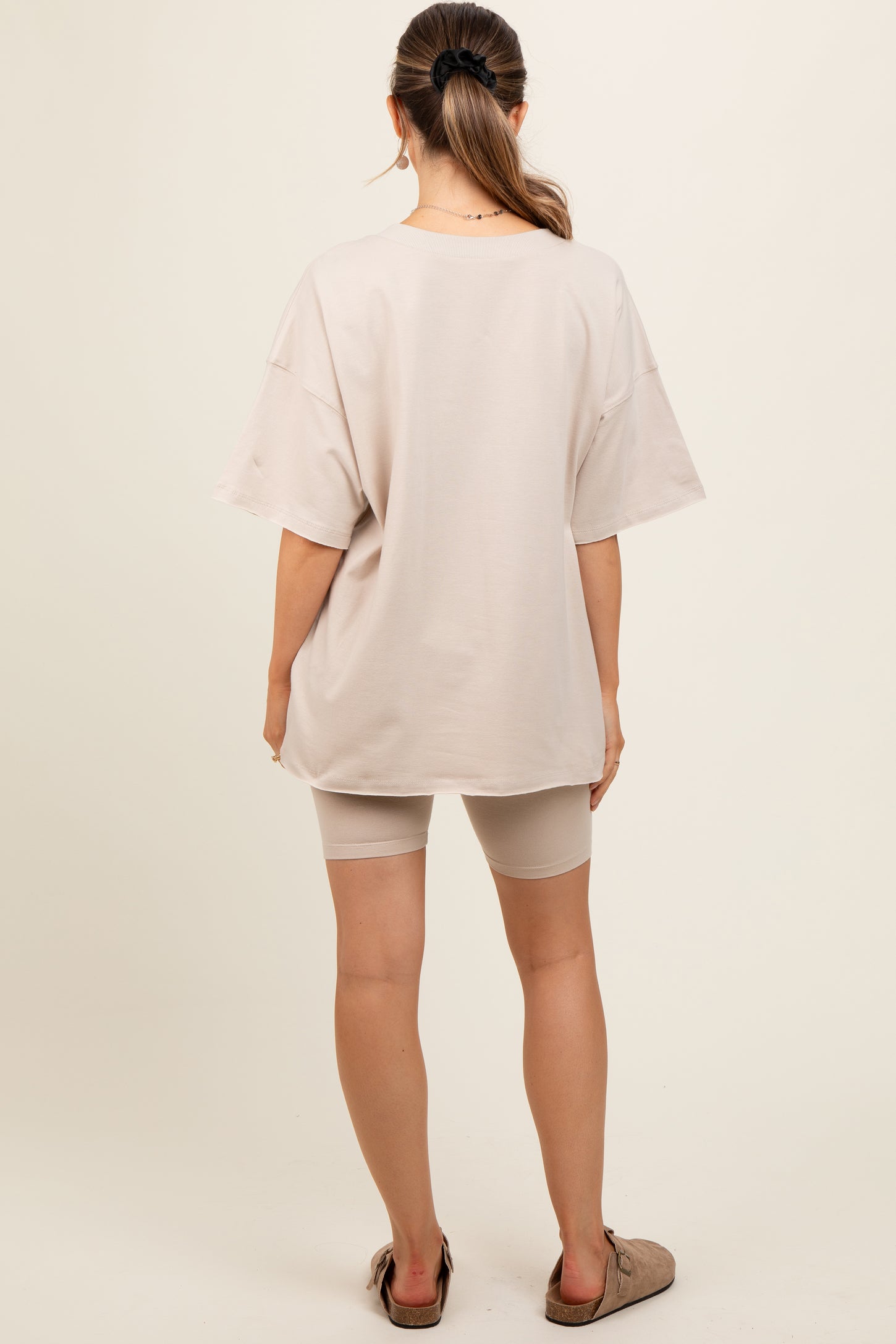 woman wearing a beige oversized t-shirt with short sleeves and beige bike shorts, showing her back, maternity wear