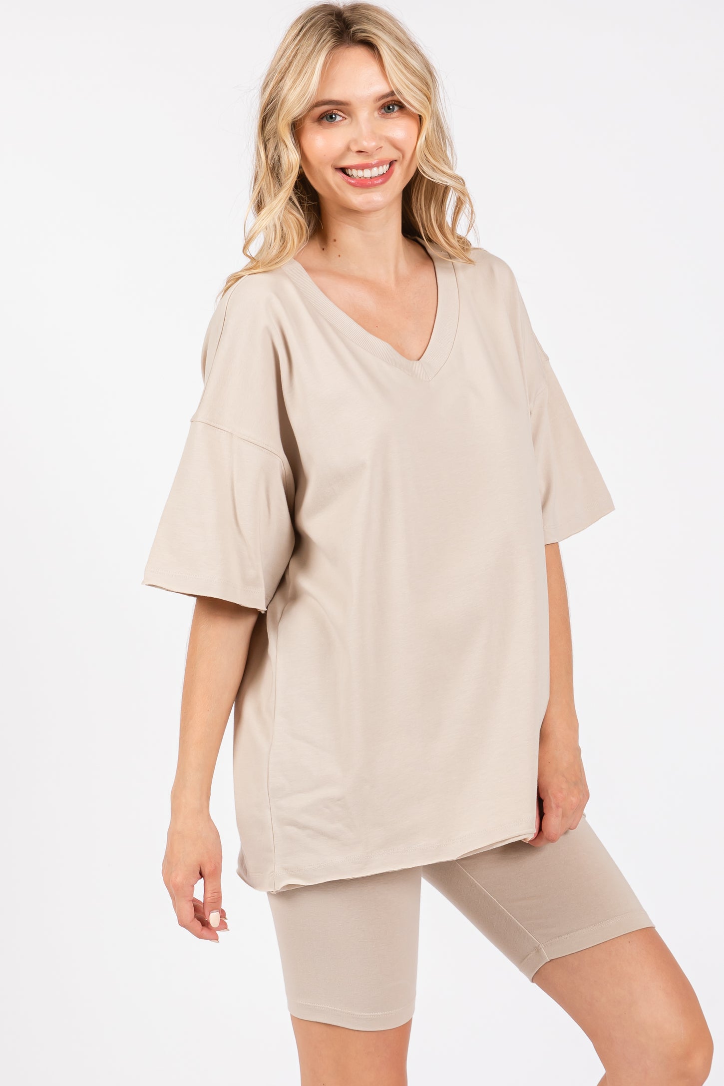 woman wearing a beige oversized v-neck t-shirt and matching bike shorts, smiling at the camera