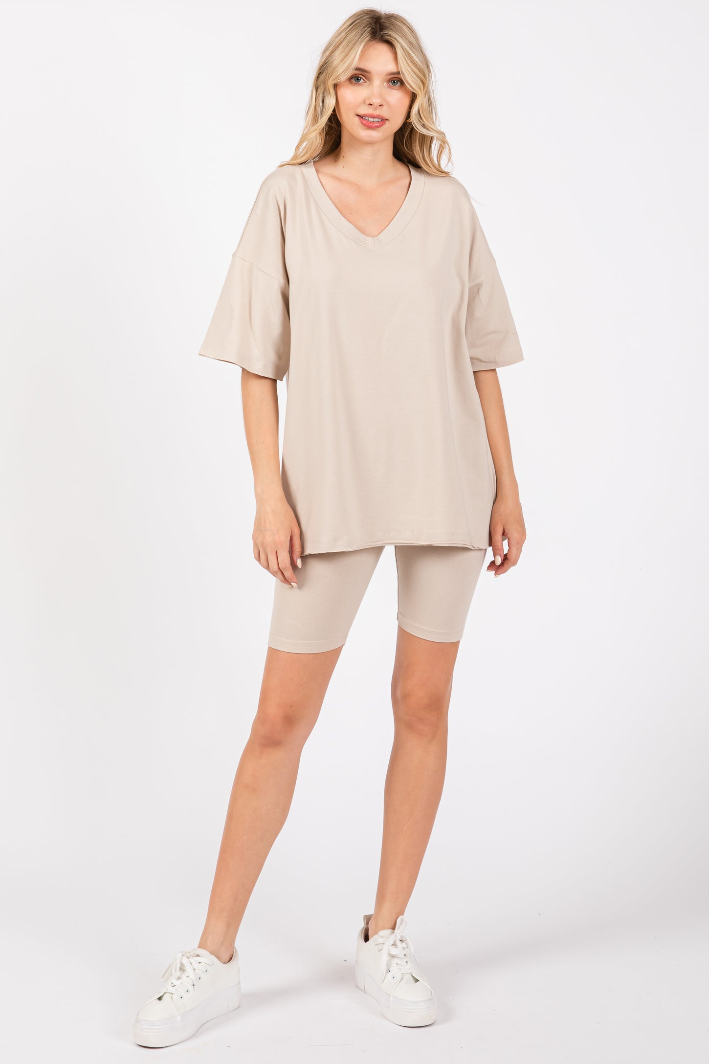woman wearing a beige oversized v-neck t-shirt and matching bike shorts with white sneakers