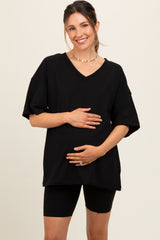 woman wearing a black v-neck maternity top and black bike shorts, holding her baby bump