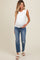 woman wearing a white ruffle sleeve maternity top and distressed blue maternity jeans, showcasing her baby bump