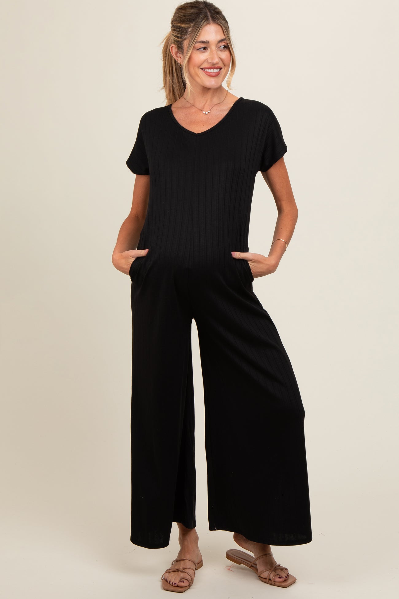 woman wearing a black ribbed maternity jumpsuit with short sleeves and side pockets