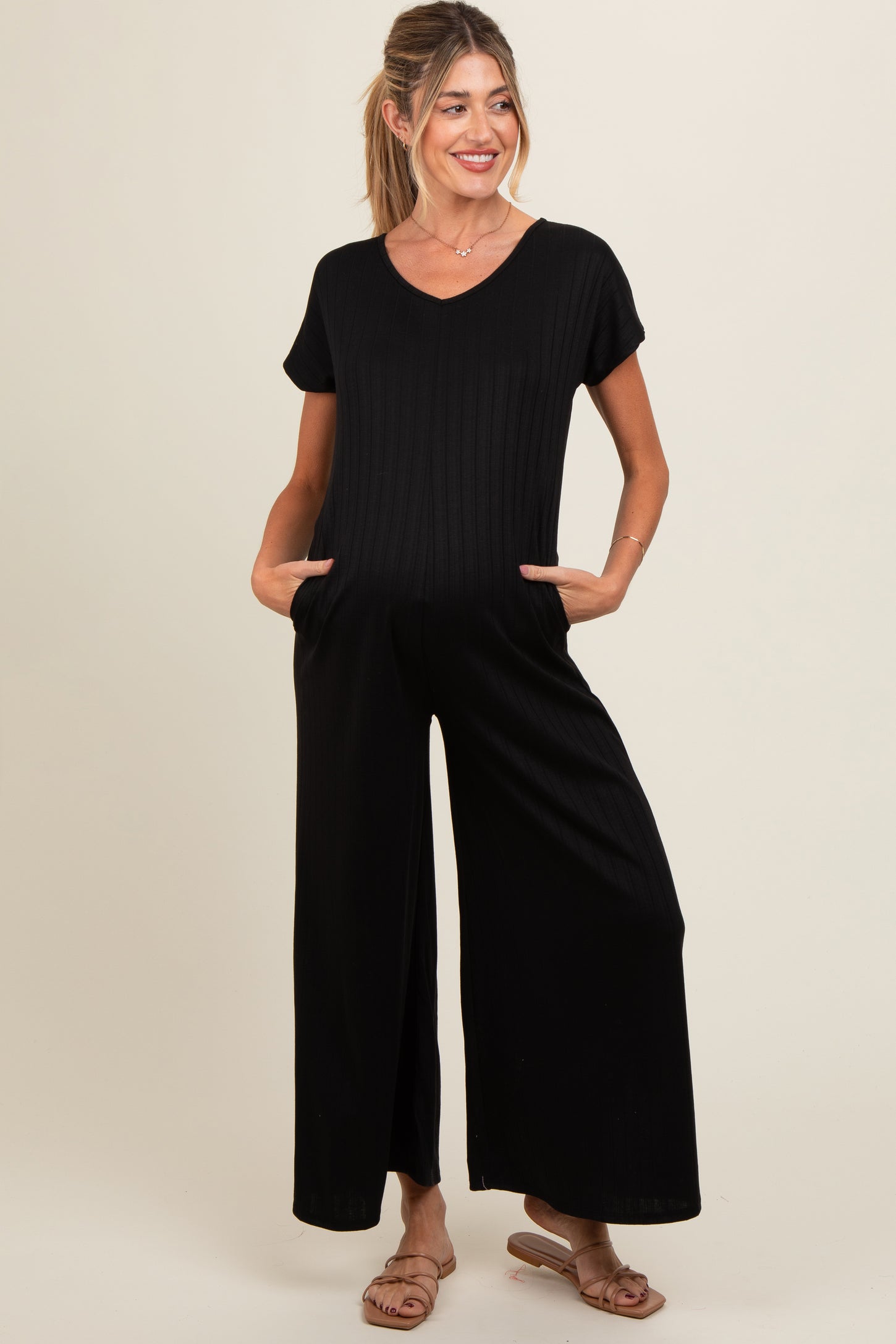 woman wearing a black ribbed maternity jumpsuit with short sleeves and side pockets