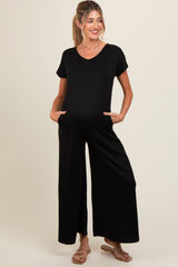 woman wearing a black ribbed maternity jumpsuit with short sleeves and side pockets