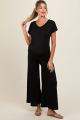 woman wearing a black ribbed maternity jumpsuit with short sleeves and wide legs, showcasing her baby bump