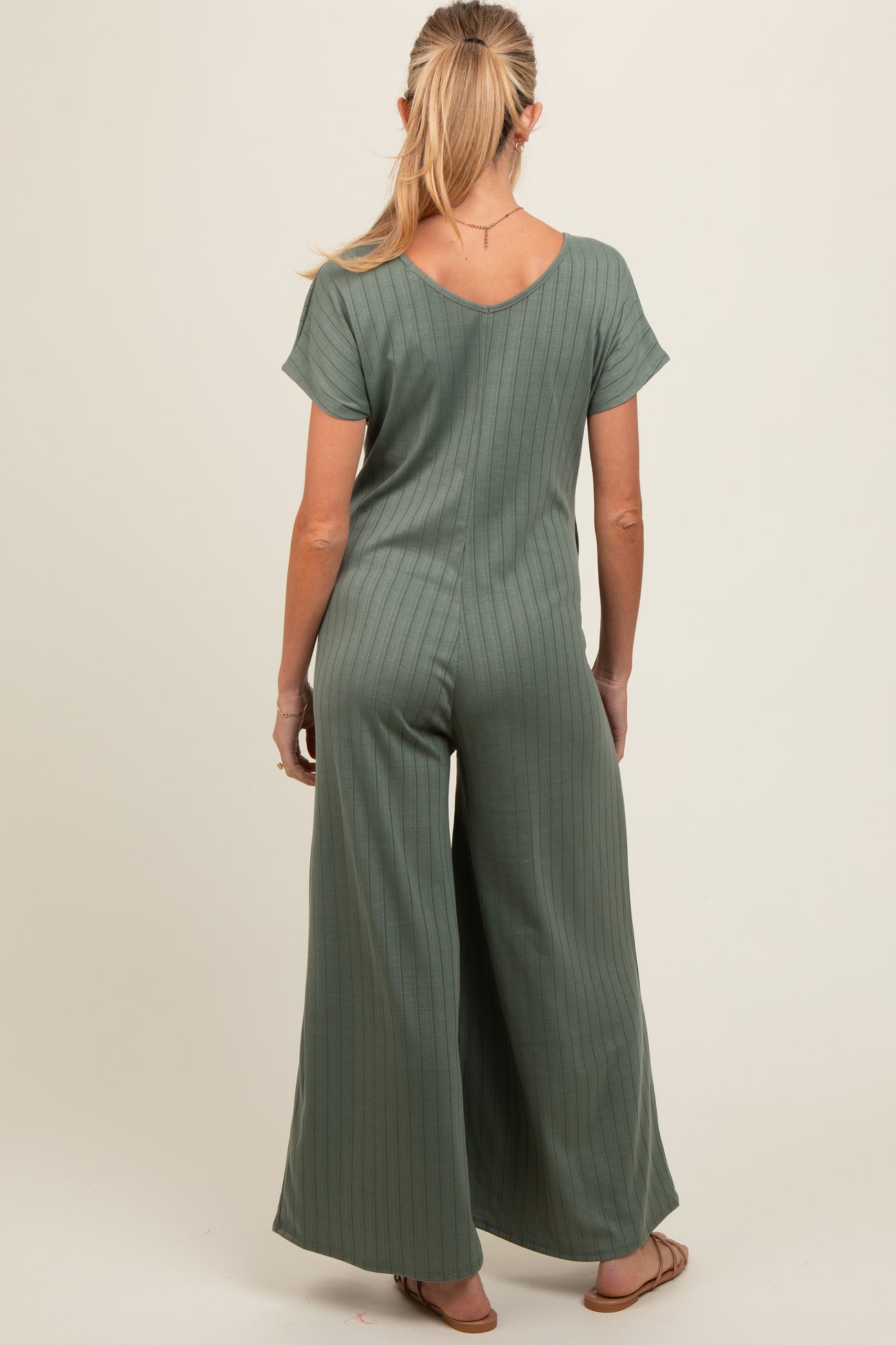 woman wearing a muted green maternity jumpsuit with short sleeves and wide leg, seen from the back