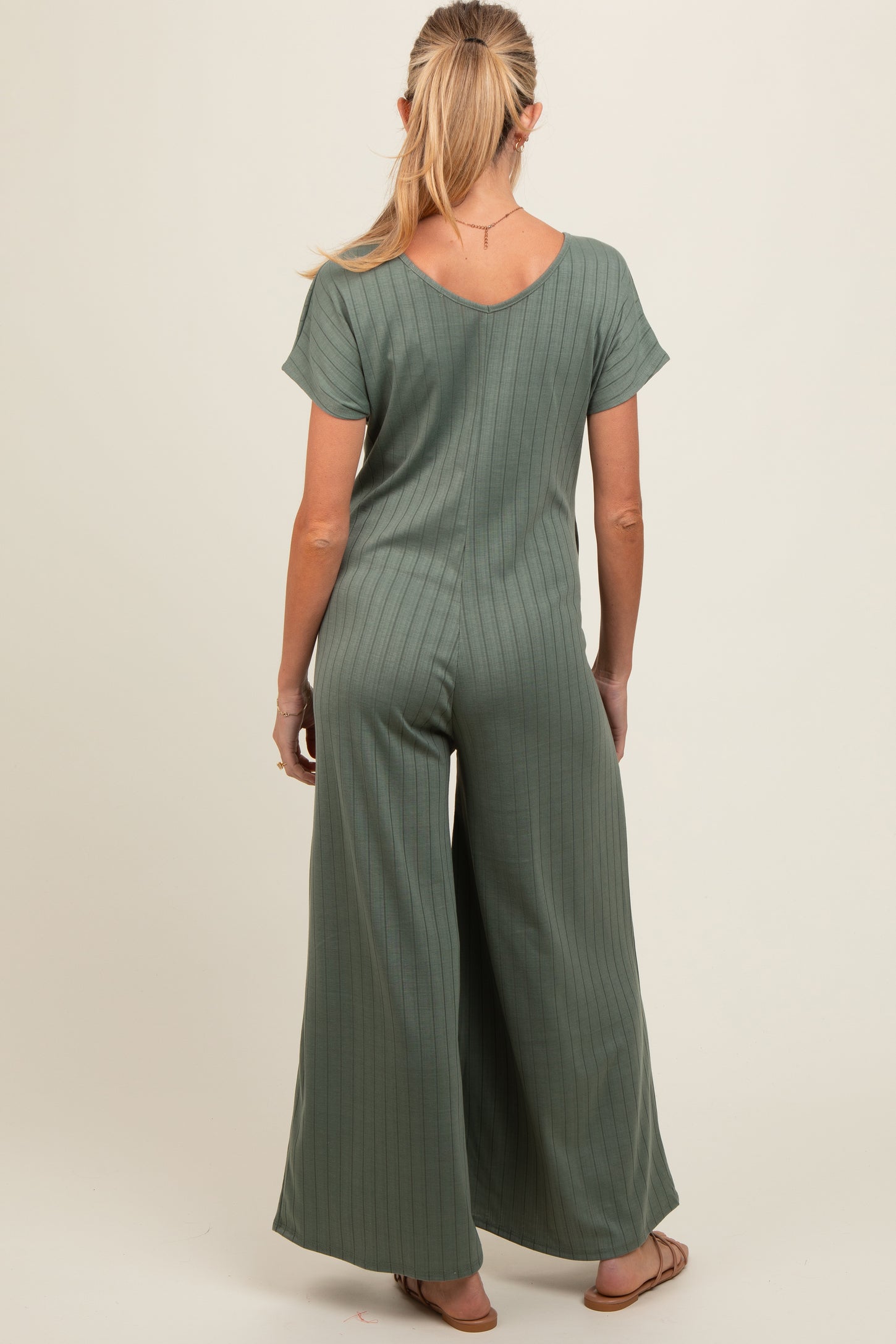 woman wearing a muted green maternity jumpsuit with short sleeves and wide leg, seen from the back