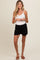 woman wearing a white tank top and black maternity shorts, holding her baby bump