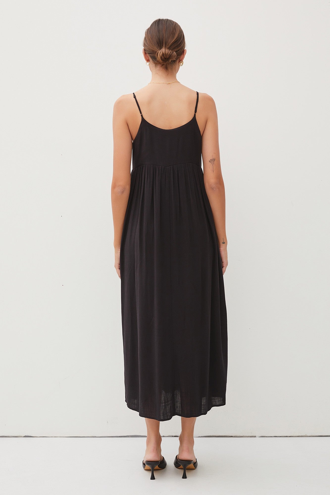 woman wearing a black spaghetti strap maxi dress with a gathered back and a flowy silhouette