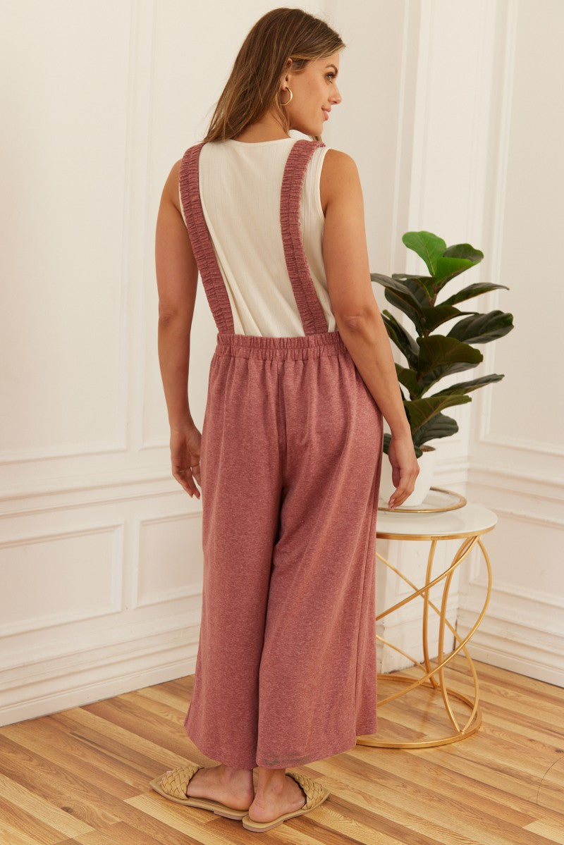 woman wearing a light pink backless jumpsuit with wide legs and a fitted bodice, standing against a backdrop of a plant