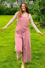 woman wearing a pink linen jumpsuit with wide legs and pockets, paired with a sheer white long sleeve top, smiling outdoors