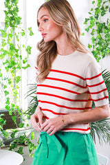 woman wearing a cream and red striped short sleeve top paired with a green skirt, standing in a bright, leafy setting