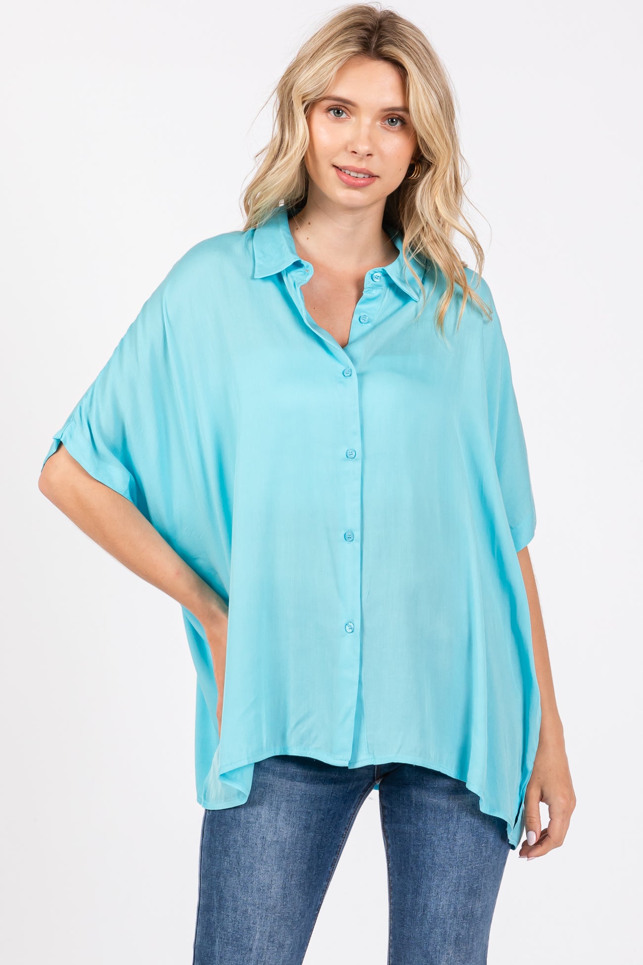 woman wearing a bright turquoise oversized button-up shirt with rolled sleeves and a relaxed fit, paired with jeans