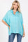 woman wearing a bright turquoise oversized button-up shirt with rolled sleeves and a relaxed fit, paired with jeans