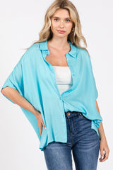 woman wearing a turquoise oversized button-up shirt with short sleeves and a white tank top, paired with high-waisted jeans