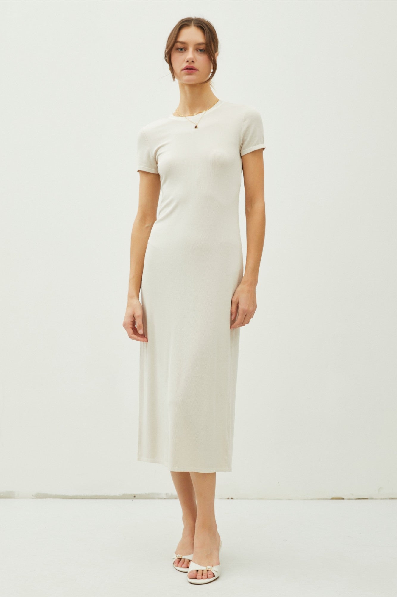 woman wearing a cream short sleeve midi dress with a fitted silhouette and a round neckline