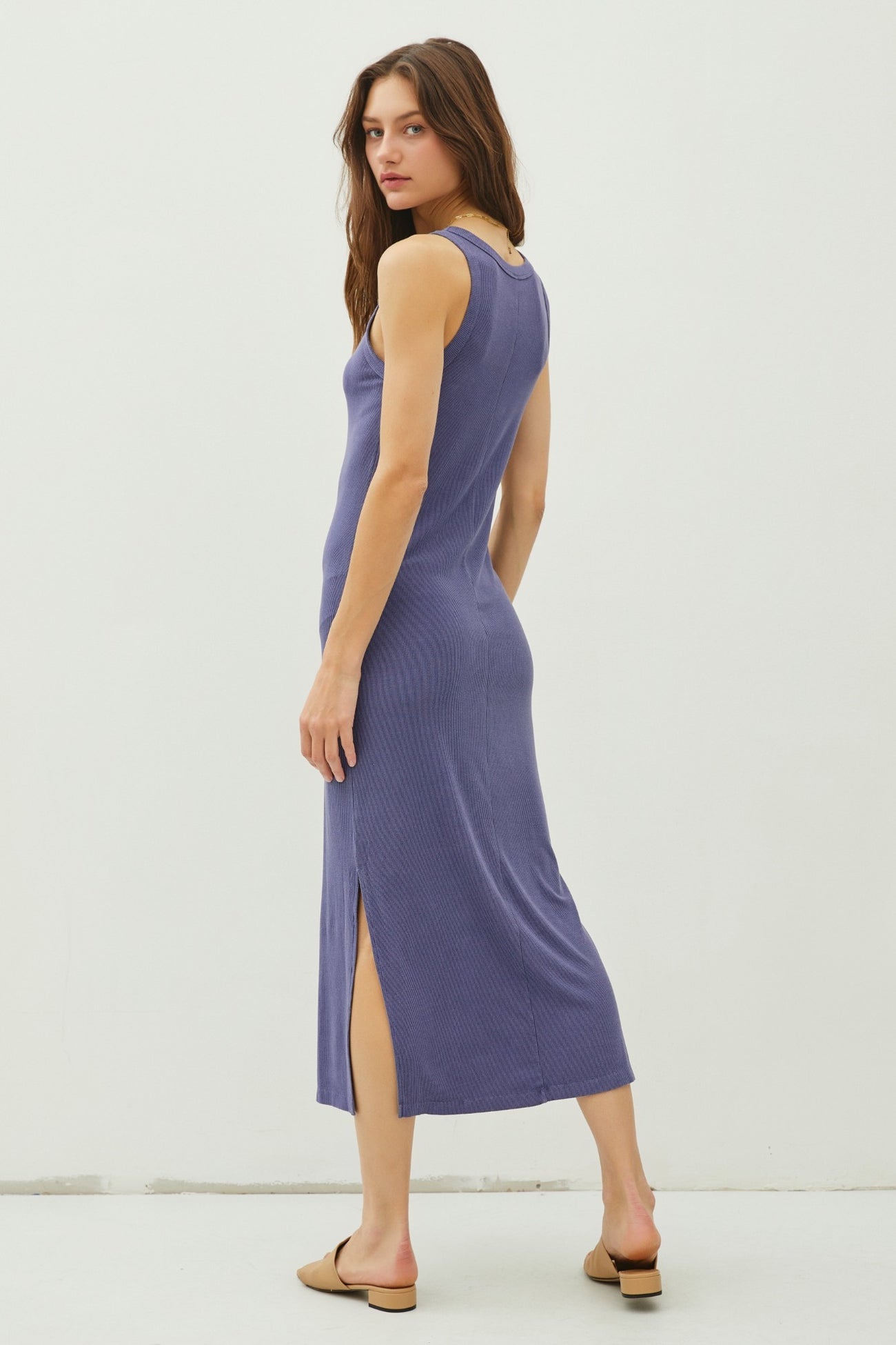 woman wearing a purple ribbed midi dress with side slits and a fitted silhouette, standing with her back to the camera