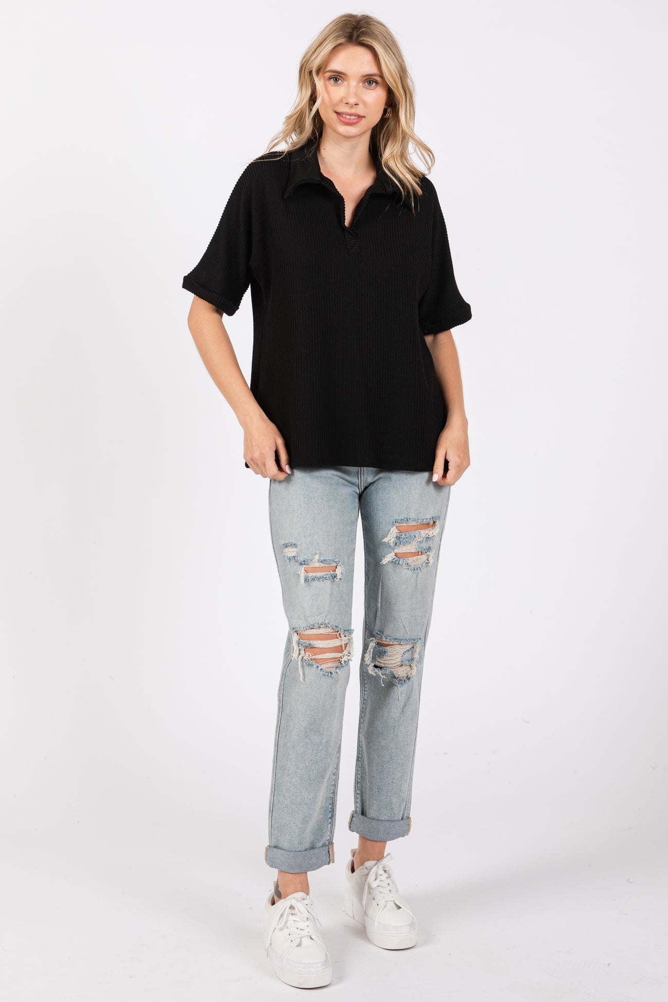 woman wearing a black short sleeve polo top and distressed light wash jeans with rolled cuffs