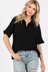 woman wearing a black short sleeve polo style top with a zipper and distressed light blue jeans