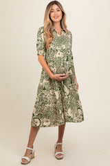 woman wearing a floral green maternity dress with a collared neck and short sleeves, holding her baby bump