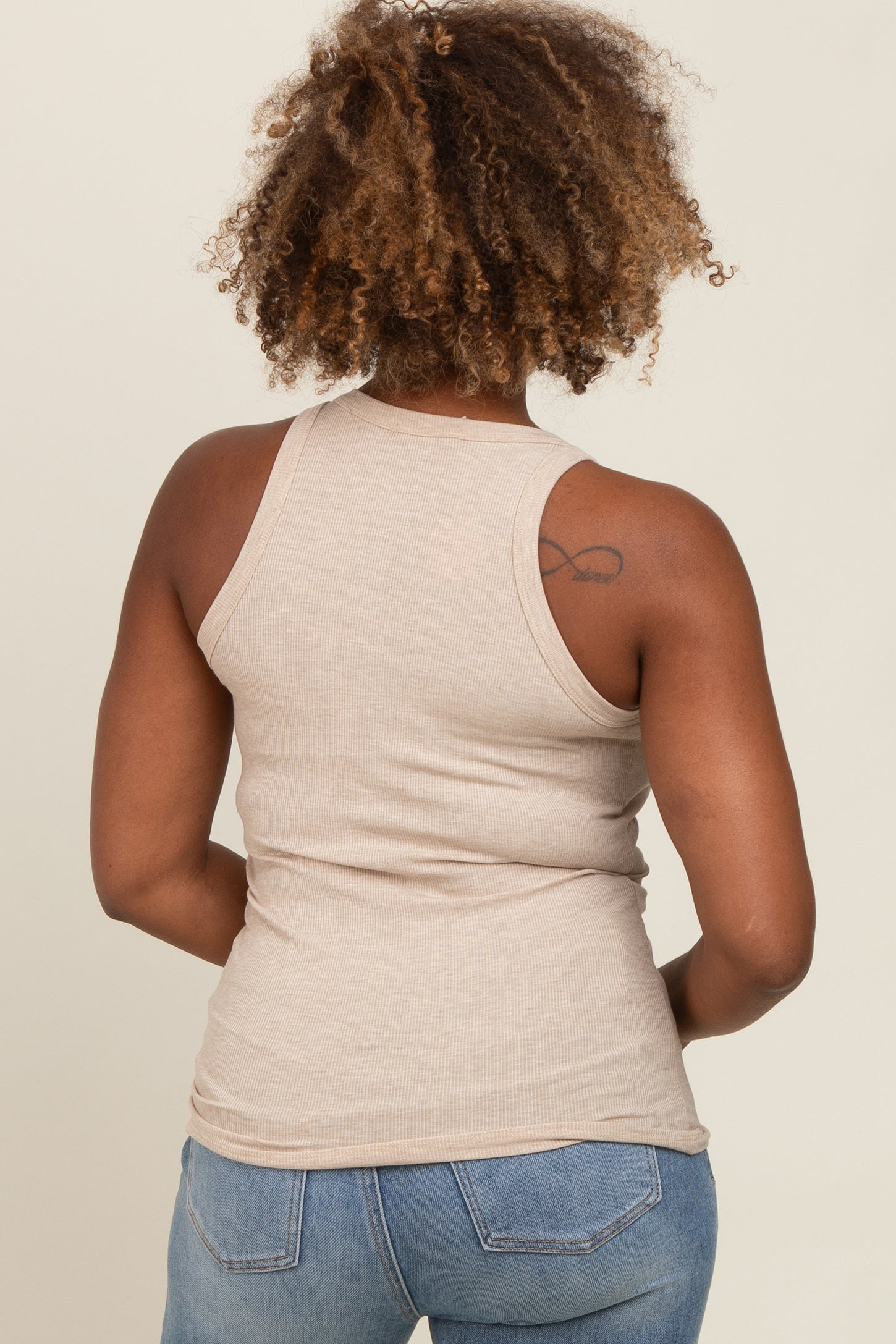 woman wearing a light beige ribbed tank top and blue jeans, seen from the back