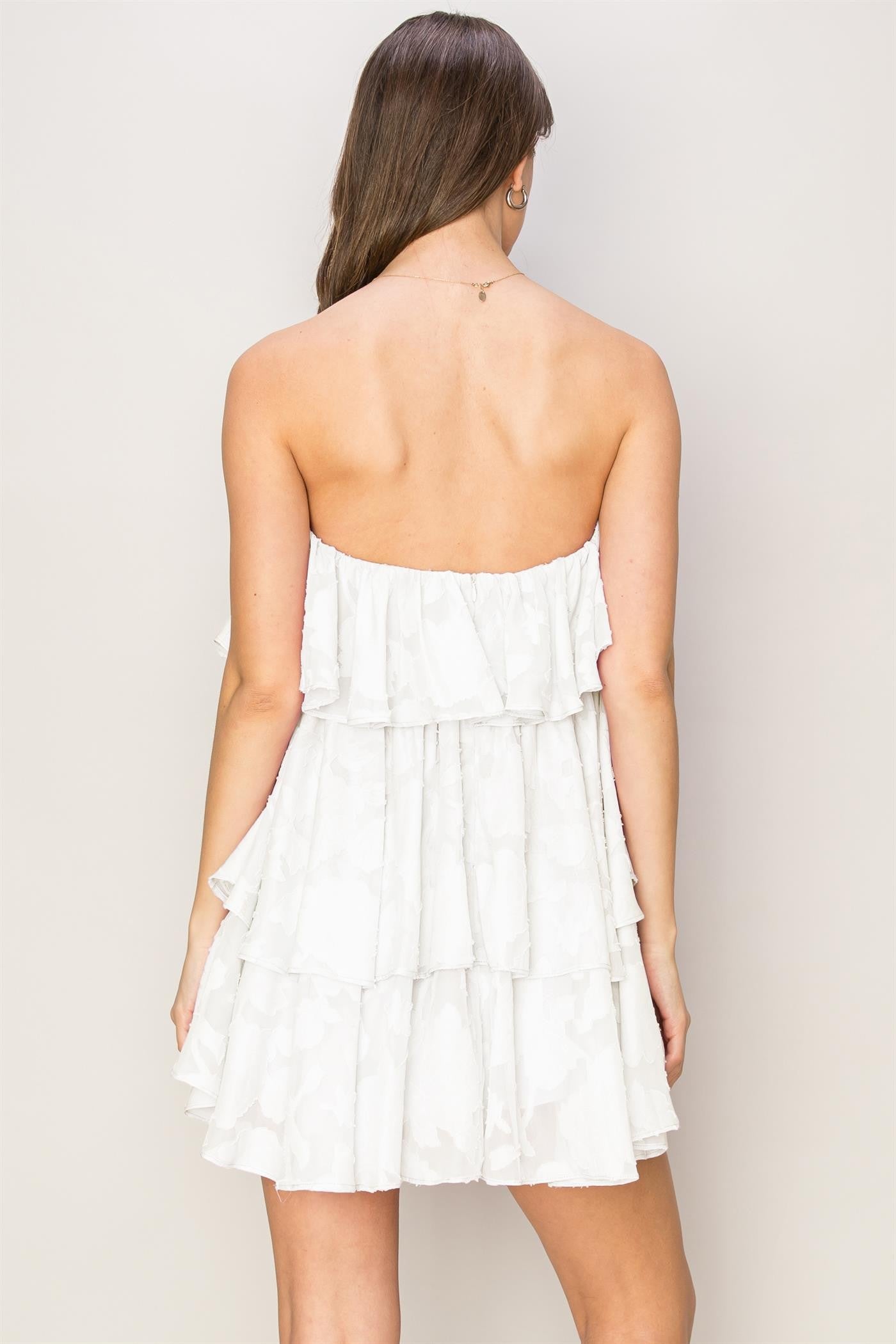 woman wearing a strapless white tiered mini dress, showing a flared silhouette and ruffled details