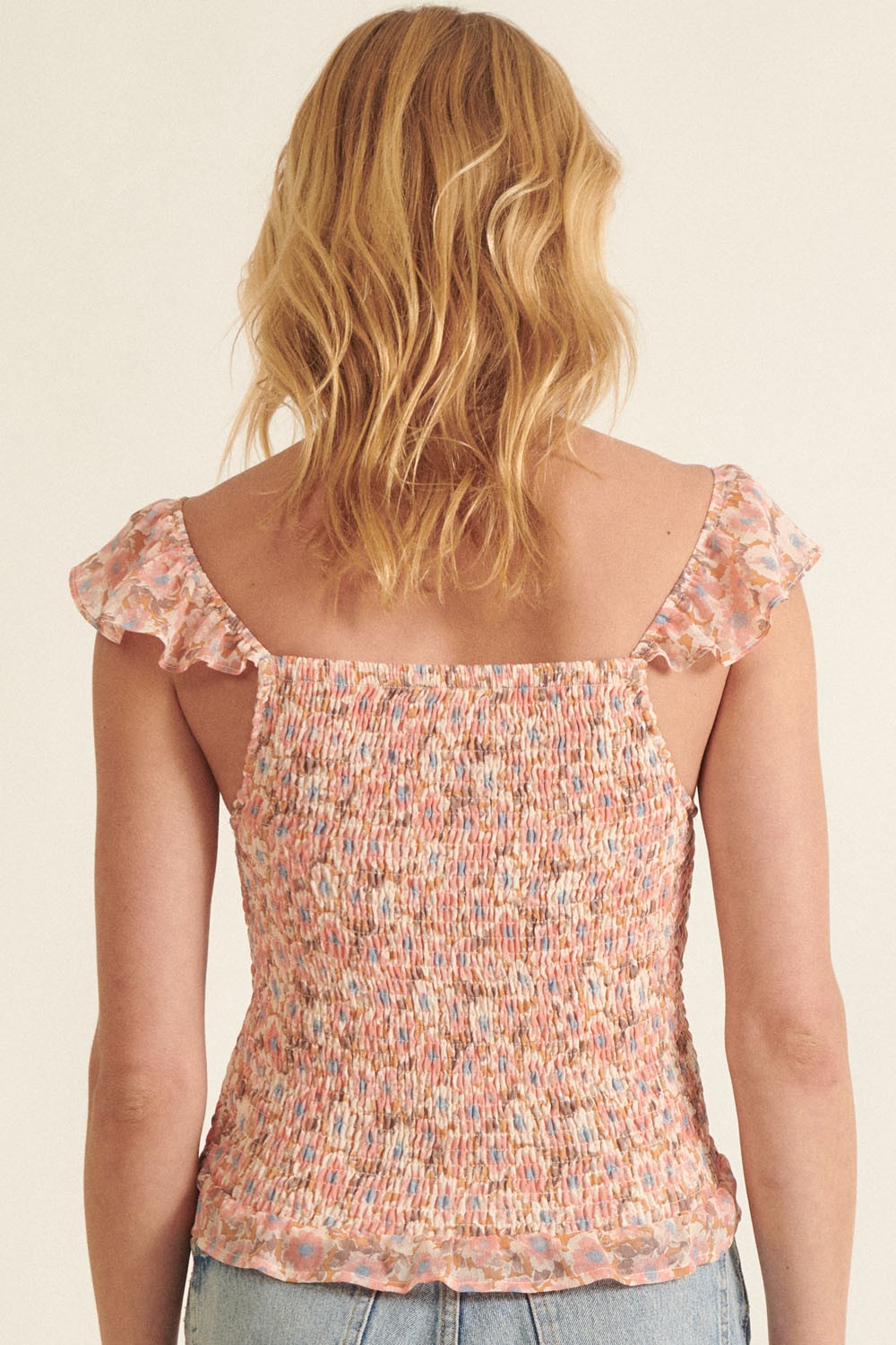 woman wearing a pink and multicolor smocked top with frilled sleeves, shown from the back