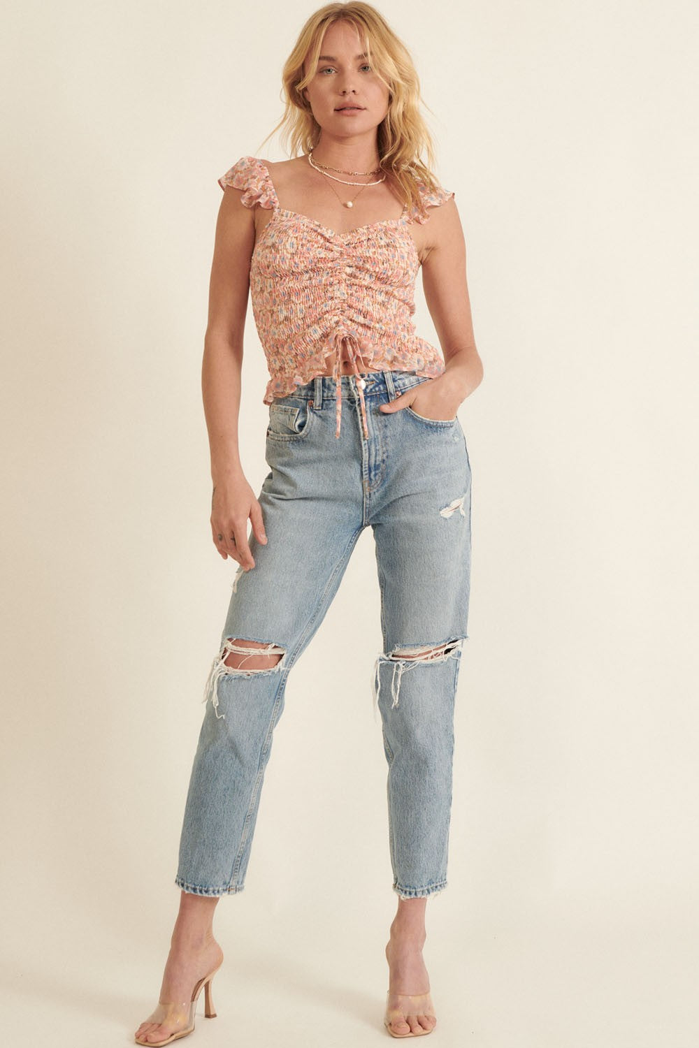 woman wearing a floral ruched crop top with ruffle sleeves and distressed light wash mom jeans