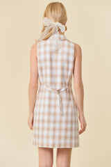woman wearing a beige and cream plaid sleeveless dress with a tie waist and a sheer hair ribbon