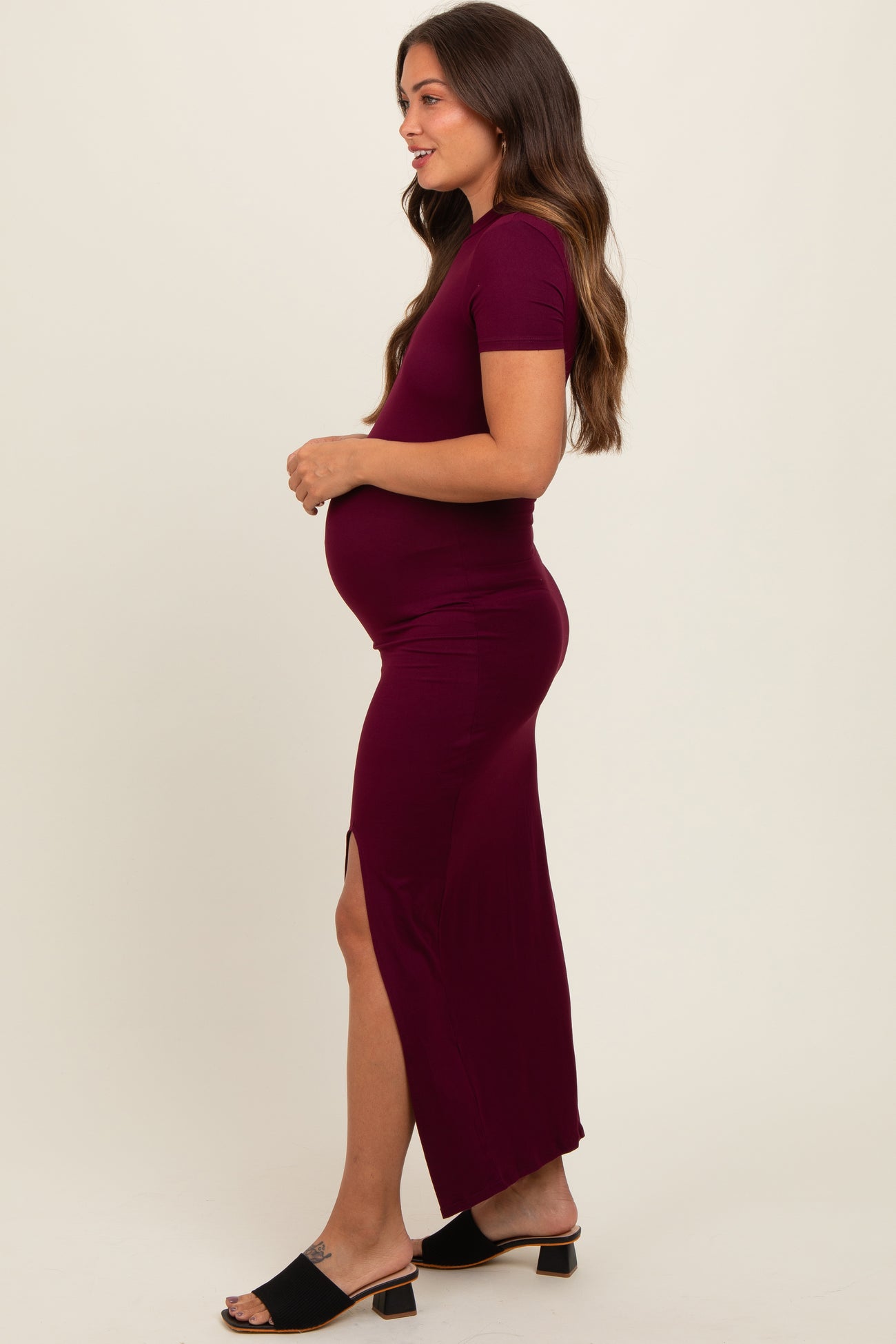 woman wearing a burgundy maternity maxi dress with short sleeves and a side slit, showing off her baby bump
