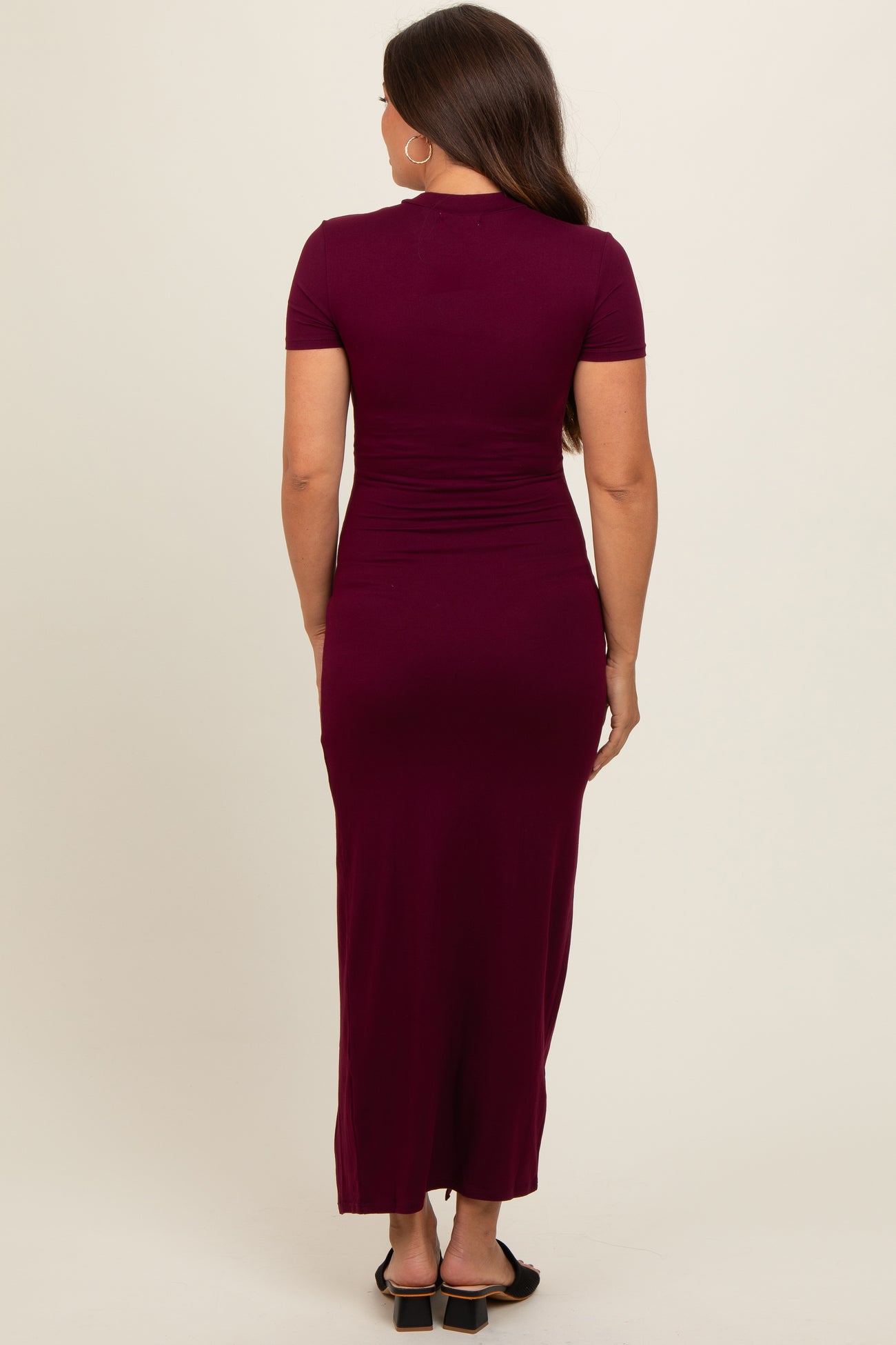 woman wearing a burgundy short sleeve maternity maxi dress, showcasing a fitted silhouette from the back
