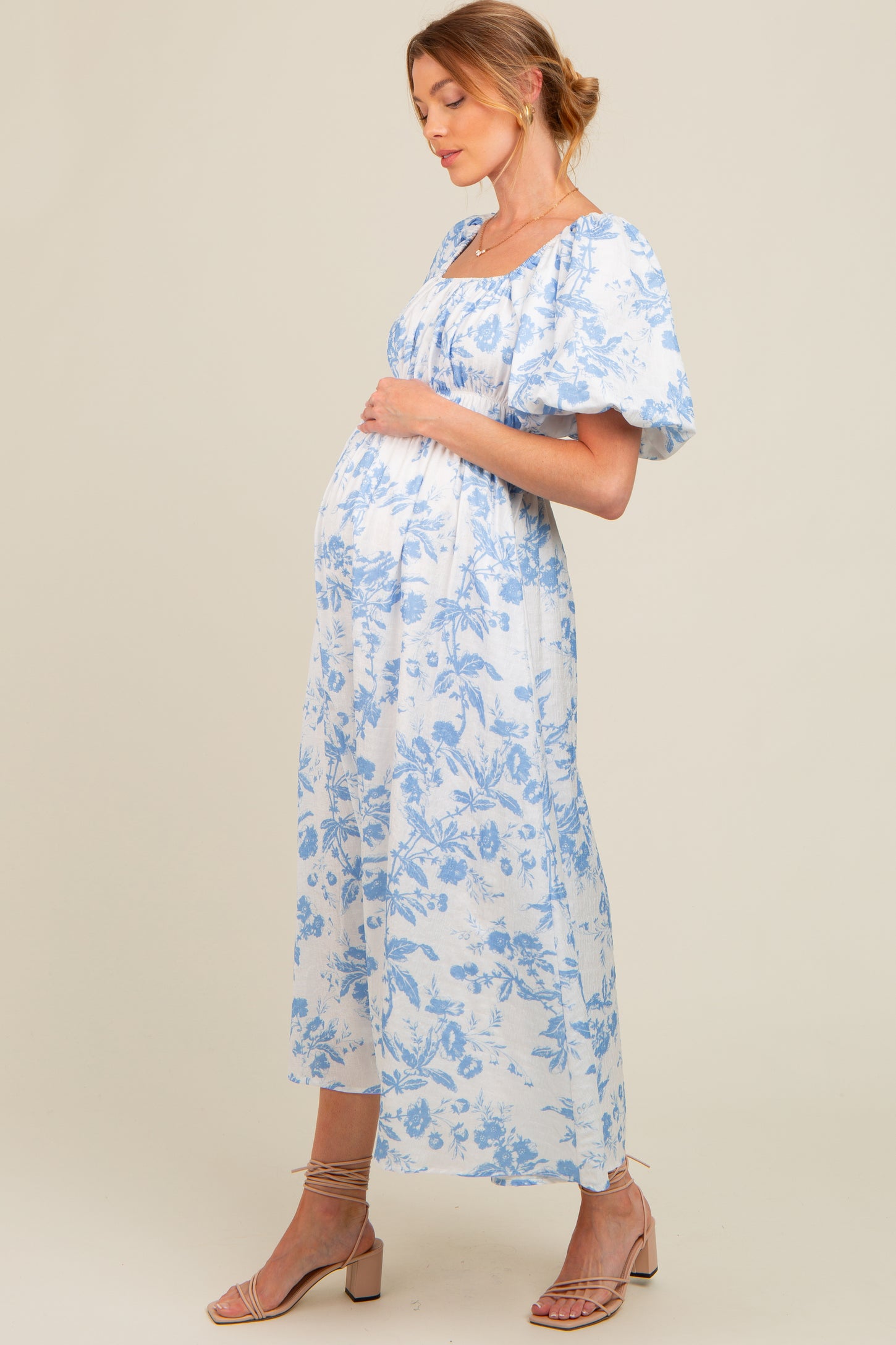 woman wearing a white floral maternity dress with blue prints and puff sleeves, showing her baby bump