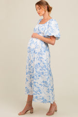 woman wearing a white floral maternity dress with blue prints and puff sleeves, showing her baby bump