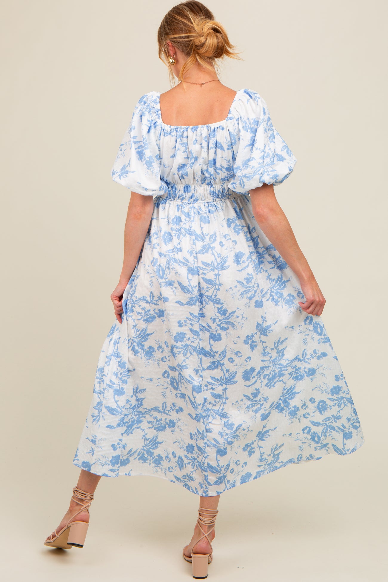 woman wearing a blue floral print maxi maternity dress with puff sleeves, showing her baby bump from the back