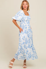 woman wearing a blue and white floral maxi dress with a square neckline and puff sleeves, featuring pockets
