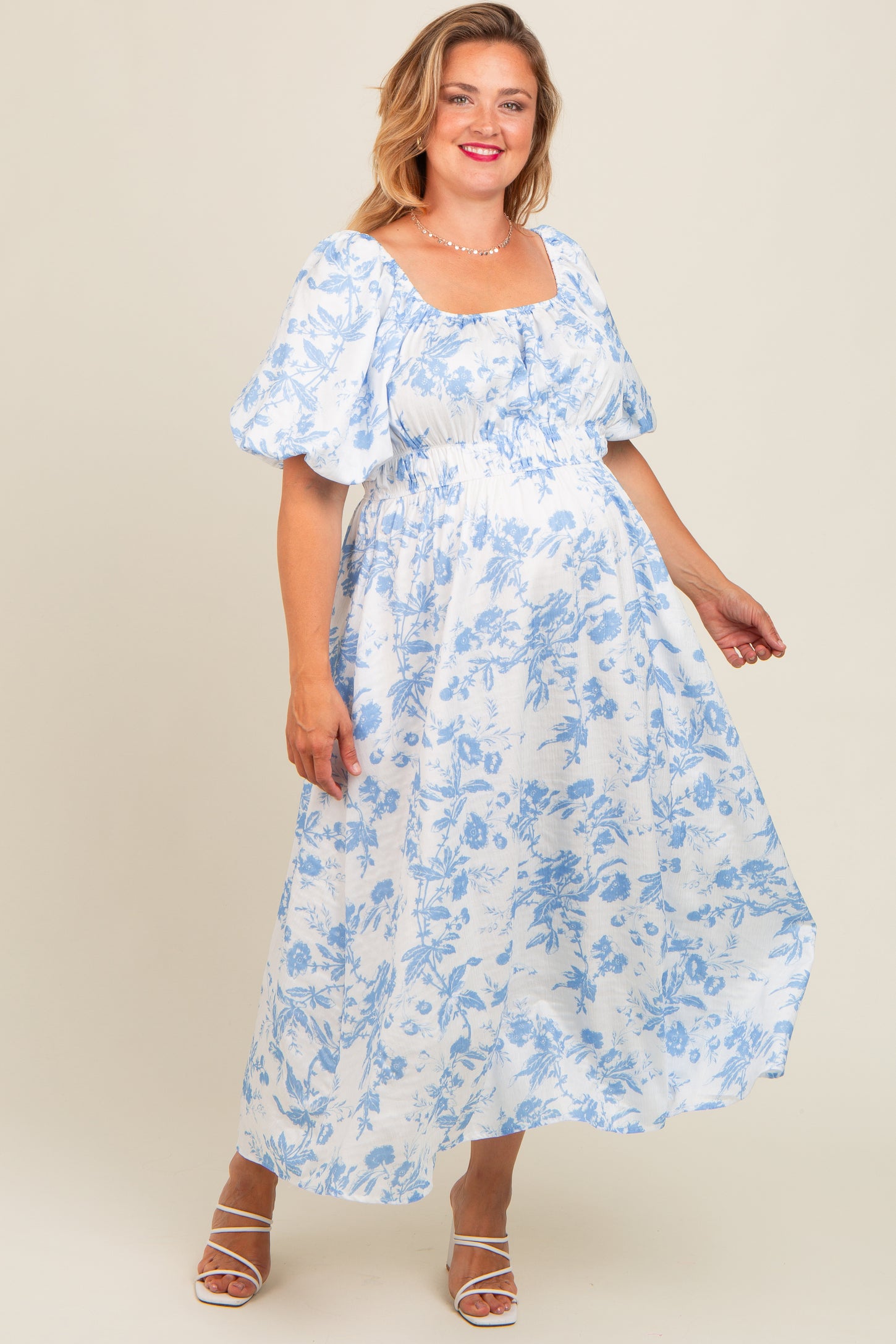 woman wearing a white floral maternity dress with short puff sleeves and a cinched waist, showing her baby bump